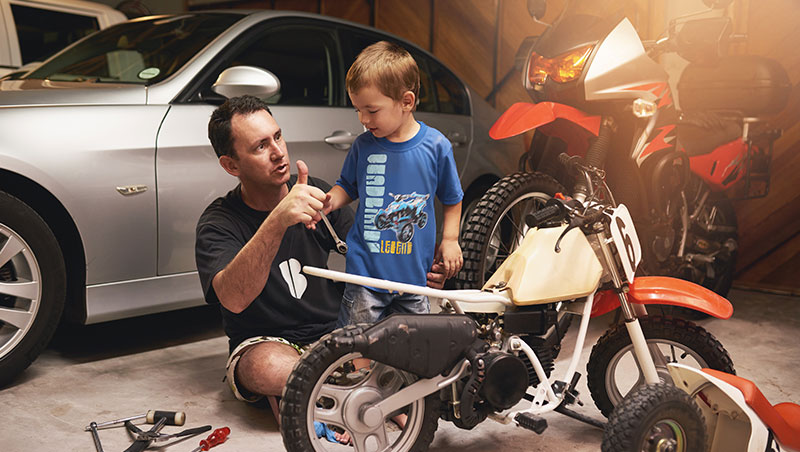 Image of a person with his kid in the garage trying to fix a small motorcycle